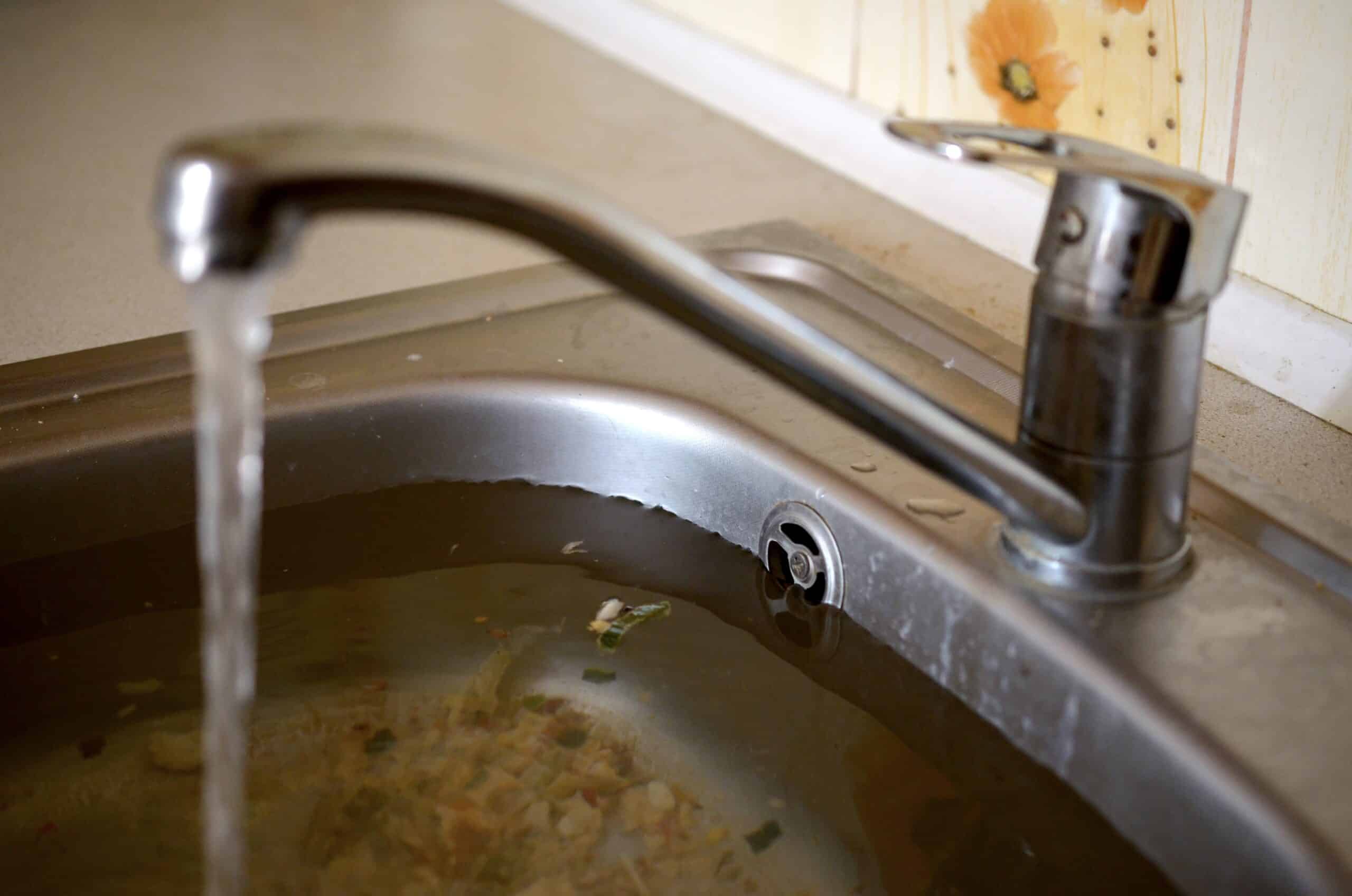 Stainless steel sink plug hole close up full of water and particles of food. Overflowing kitchen sink, clogged drain.